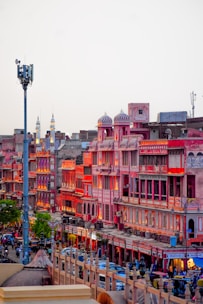A vibrant market street in Jaipur, India, featuring traditional Rajasthani architecture with pink and red buildings illuminated by warm lighting. The street is bustling with people, vehicles, and shops creating an energetic urban atmosphere.
