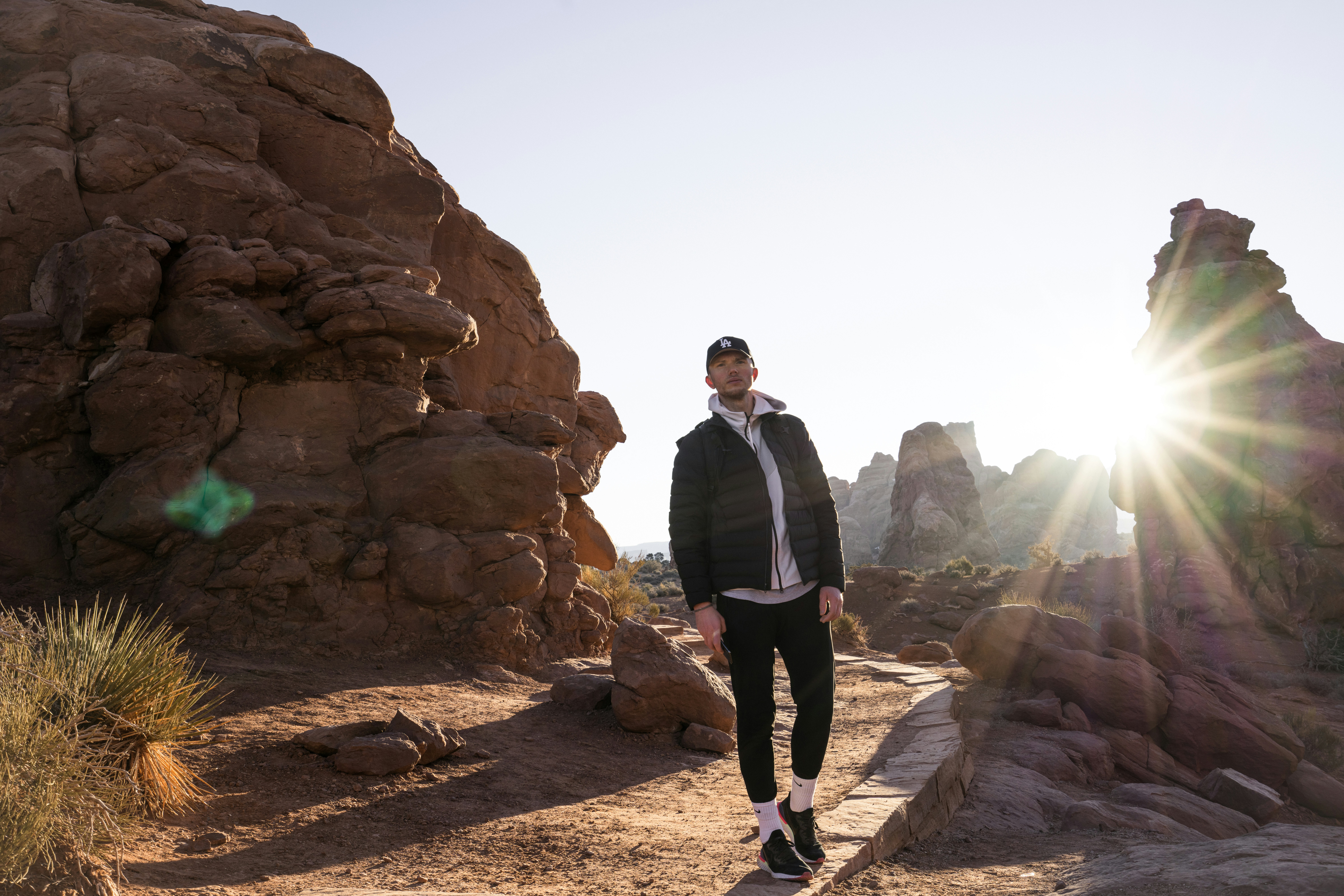 a man standing in front of a rock formation, Hiking during sunrise at Arches National Park near Moab, UT, in January