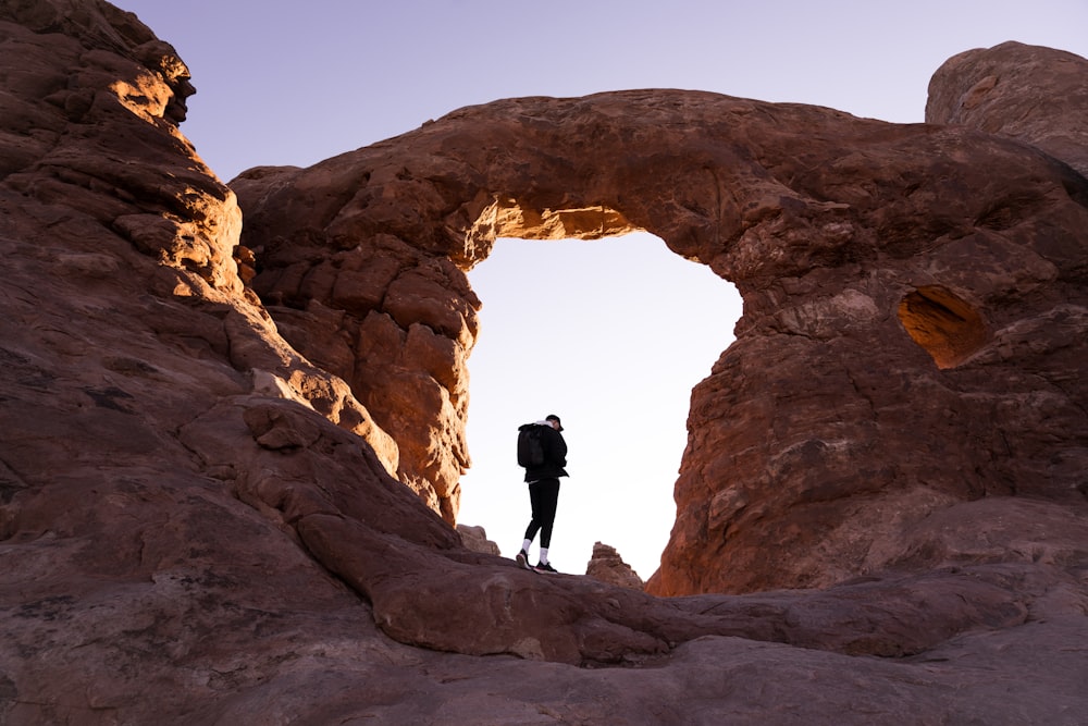 a person standing in a large rock cave with Arches National Park in the background