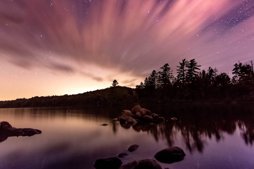 a body of water with trees and a colorful sky above