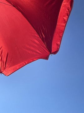 Vibrant red umbrella opened wide against a bright blue sky