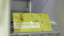 A sign is displayed with yellow and white colors featuring the text 'ELETRONIC TEMP. CONTROL' along with 'Soft Touch Digital Display.' The background has a soft yellow hue with circular patterns resembling bubbles or holes. The brand 'Homa' is visible along with a 20th-anniversary symbol.