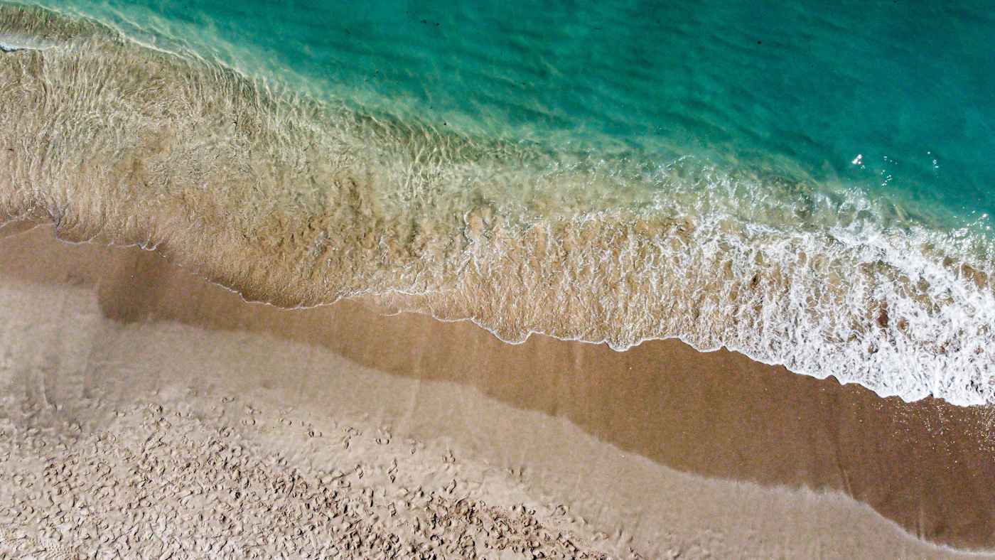 Waves rolling onto a sandy beach, seen from above.