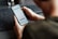 A person is holding a smartphone in their hand, focusing on a timer or scheduling app displayed on the screen. The person's arm and part of the torso are visible. The setting appears to be a workspace with a keyboard slightly out of focus in the background.