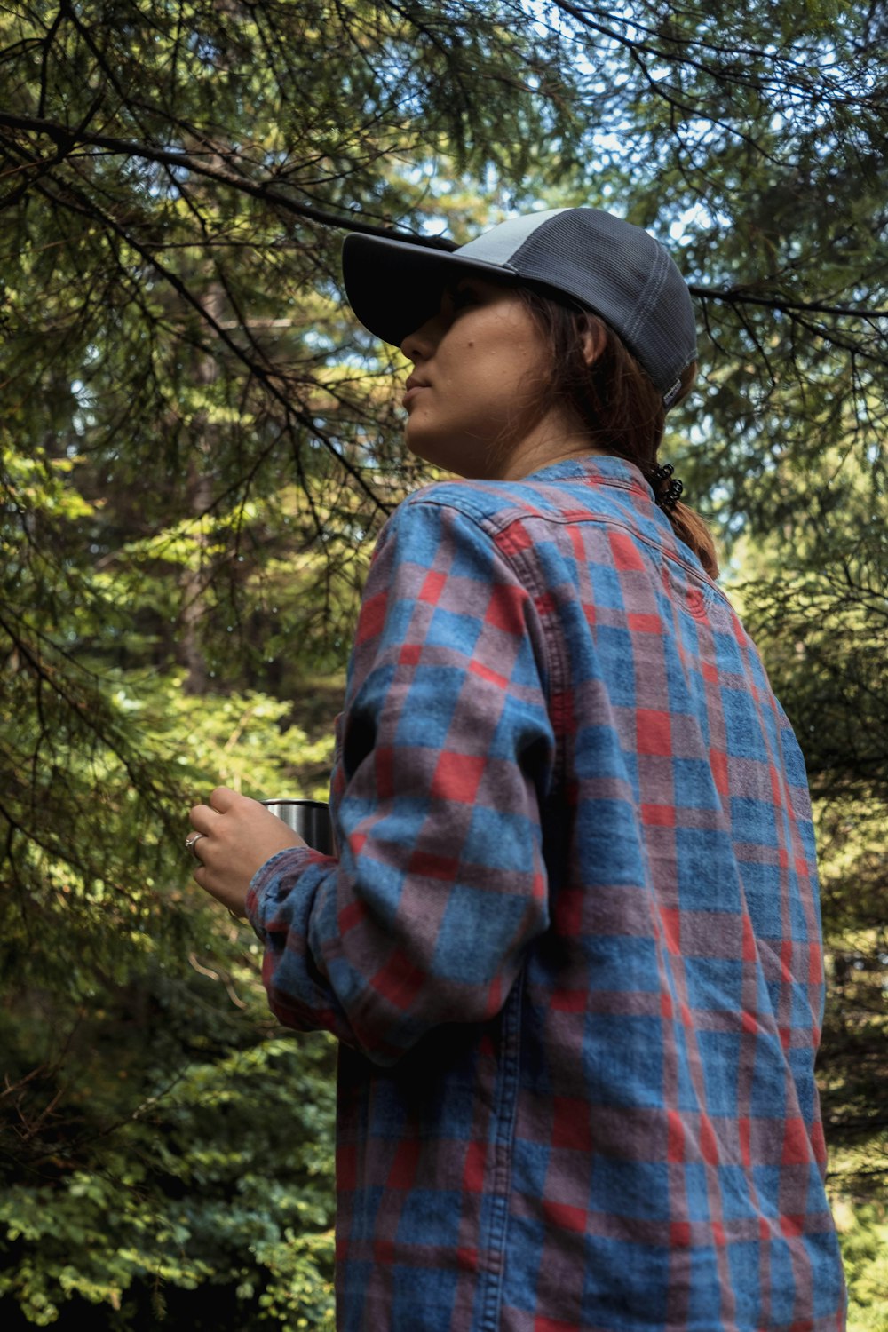a man in a hat and plaid shirt standing in front of trees