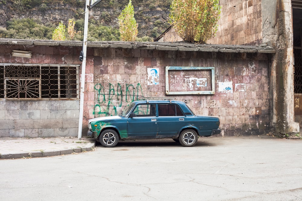 a blue car parked in front of a building with graffiti on it