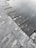 A close-up view of a tiled surface with dark, slate-like stones arranged in a neat pattern. Part of the surface is submerged under shallow water, creating a reflective effect. The textures of the stones are varied, with some showing light veining and natural blemishes.
