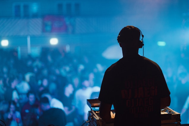 A lively urban music event with a DJ mixing tracks in front of an enthusiastic crowd.