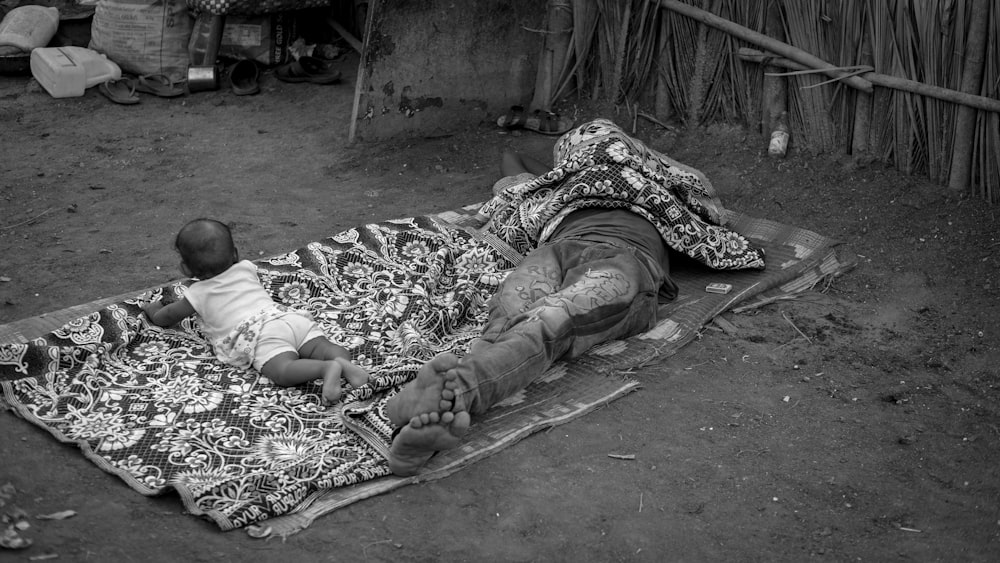 a person and a child lying on a blanket on the ground