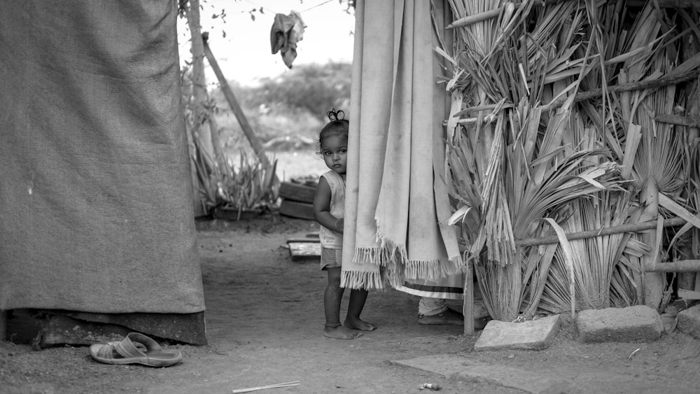 a young girl standing next to a tall grass hut