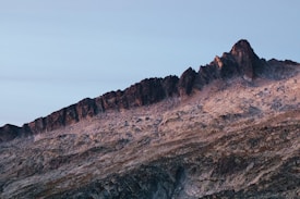 A rugged mountain range with sharp peaks and rocky terrain. The image captures the natural beauty of the landscape as the sunlight casts warm hues on the rocks, contrasting with the cold tones of the sky.