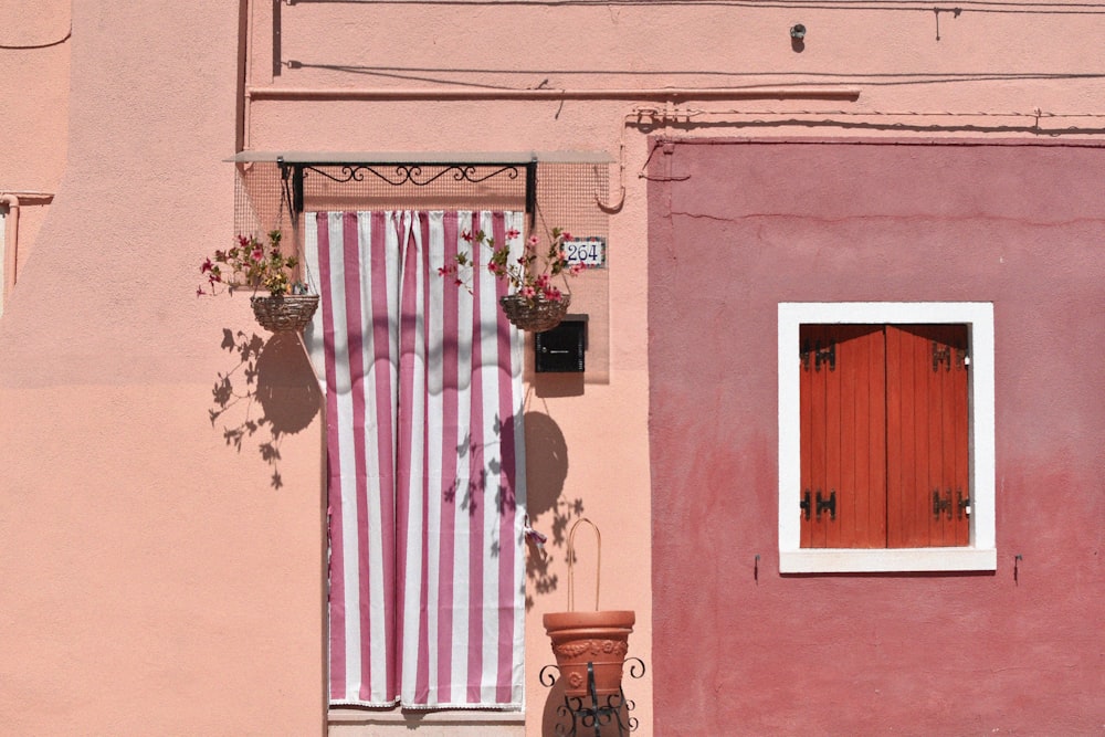 a pink building with a window and potted plants