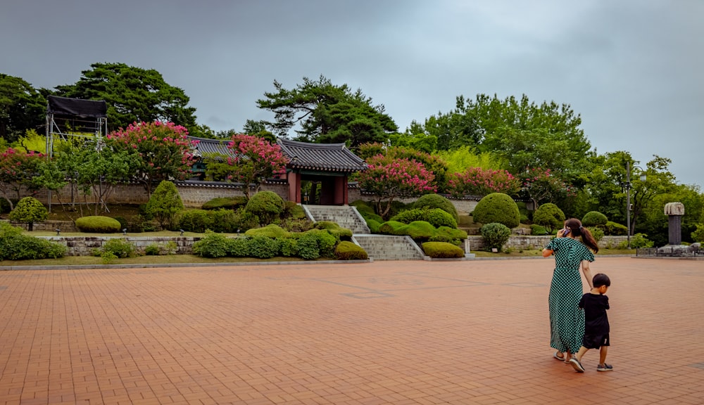 a man and a child walking on a brick path in front of a garden