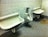 A public restroom with two wall-mounted urinals and a sink on a concrete floor. The walls are made of light-colored stone tiles, and there are visible stains and discoloration on the floor.