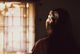 A woman gently massaging herbal oil into her scalp, sunlight streaming through a window.
