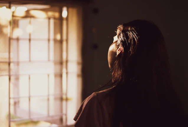 A woman gently massaging herbal oil into her scalp, sunlight streaming through a window.