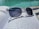 A pair of transparent sunglasses with dark lenses rests on an open book with printed text, positioned near a swimming pool. The sunlight creates reflections on the water and the surface of the book.