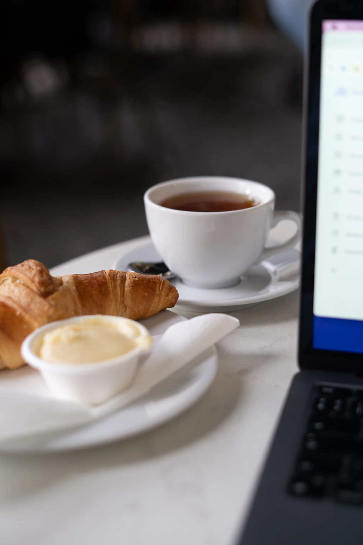 A laptop beside coffee and pastries on a café table