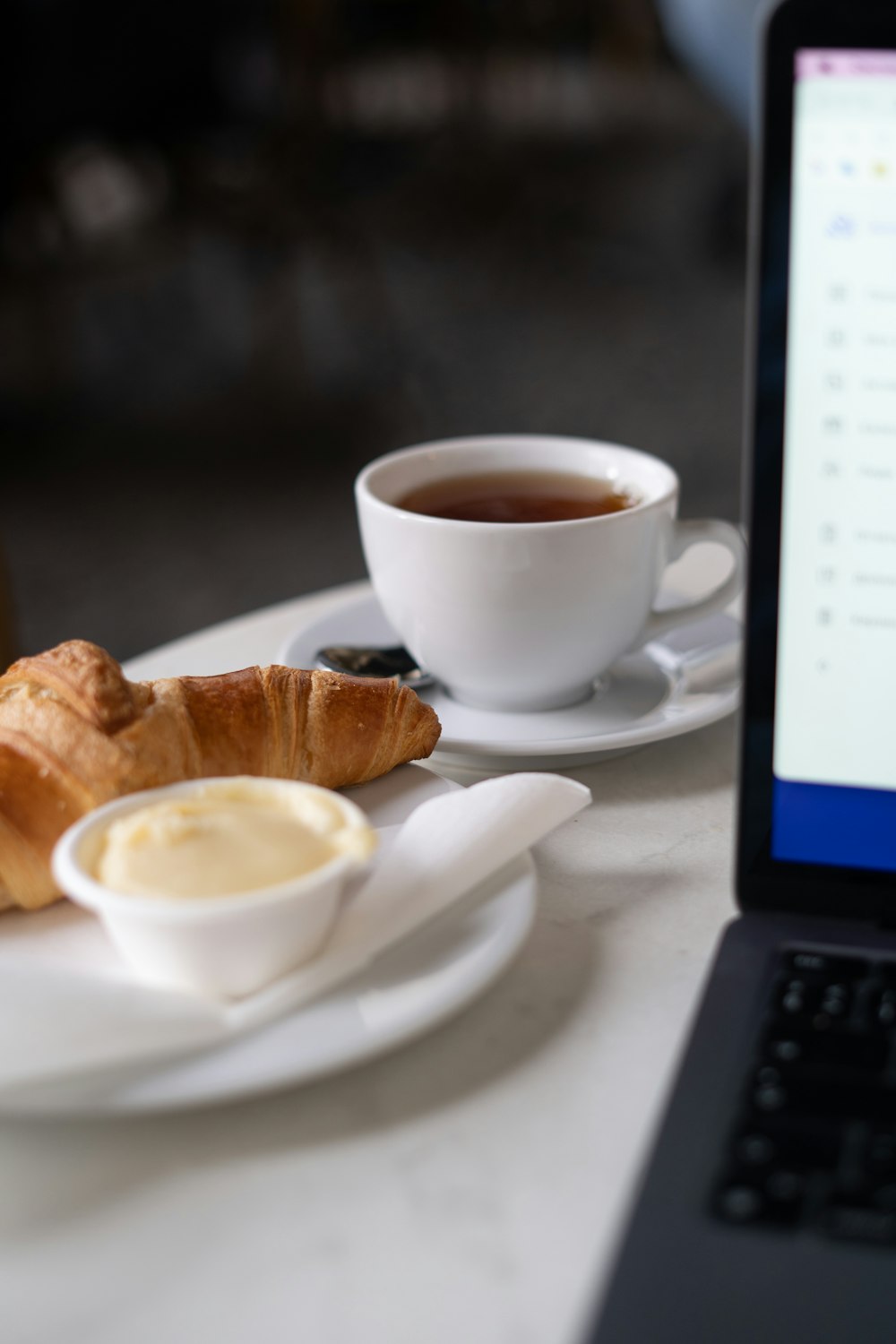 a cup of coffee next to a plate of pastries and a laptop