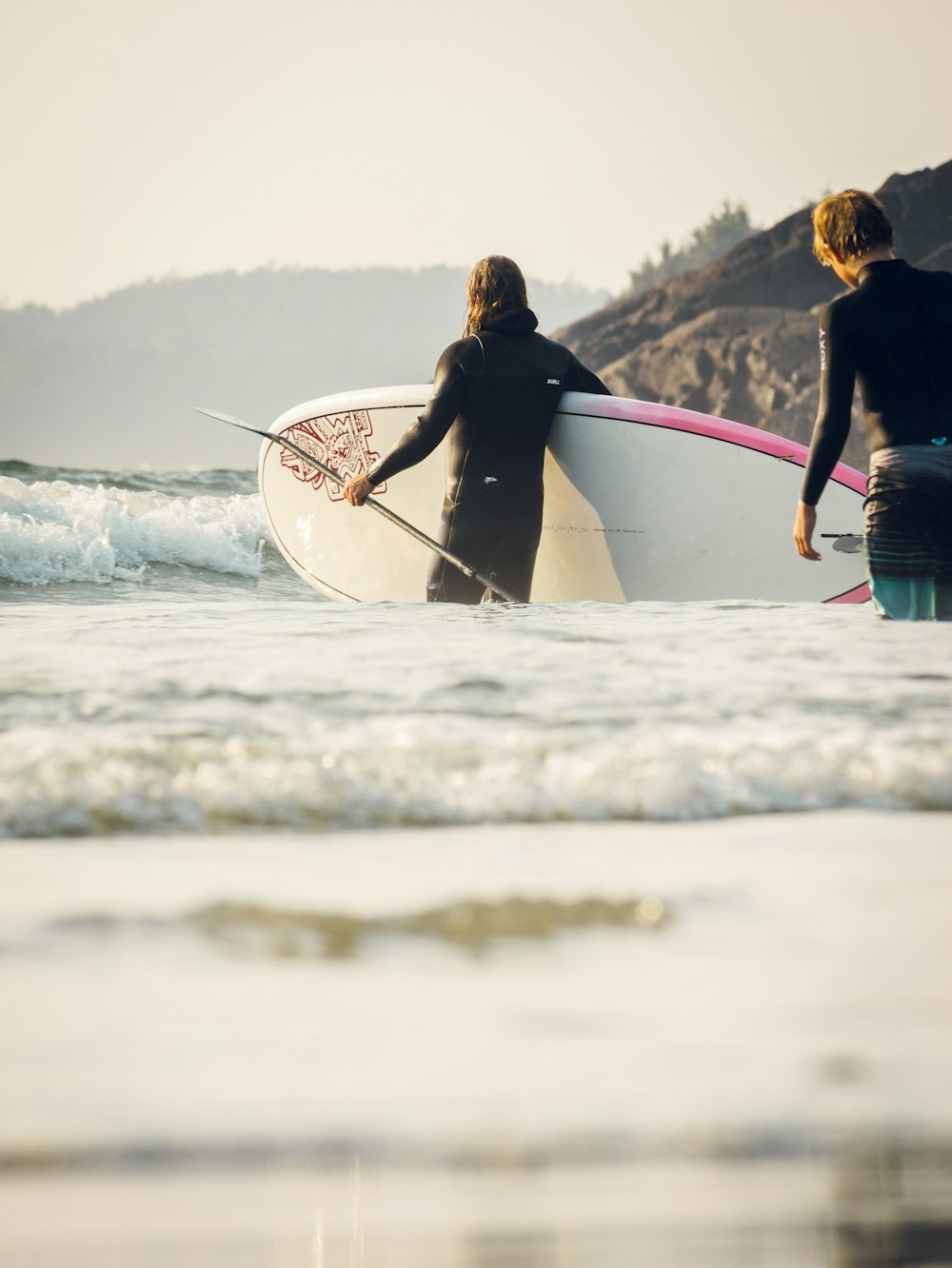 a couple of people walk across the water with surfboards