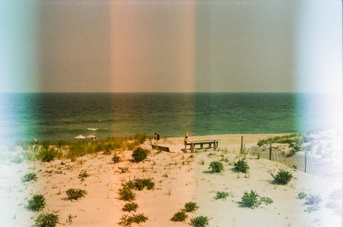 A beach with a wooden bench overlooking calm water under a clear sky.