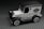 A miniature vintage car model with ornate detailing, featuring a black roof, white body, and classic design elements. The car is displayed on a textured gray base.