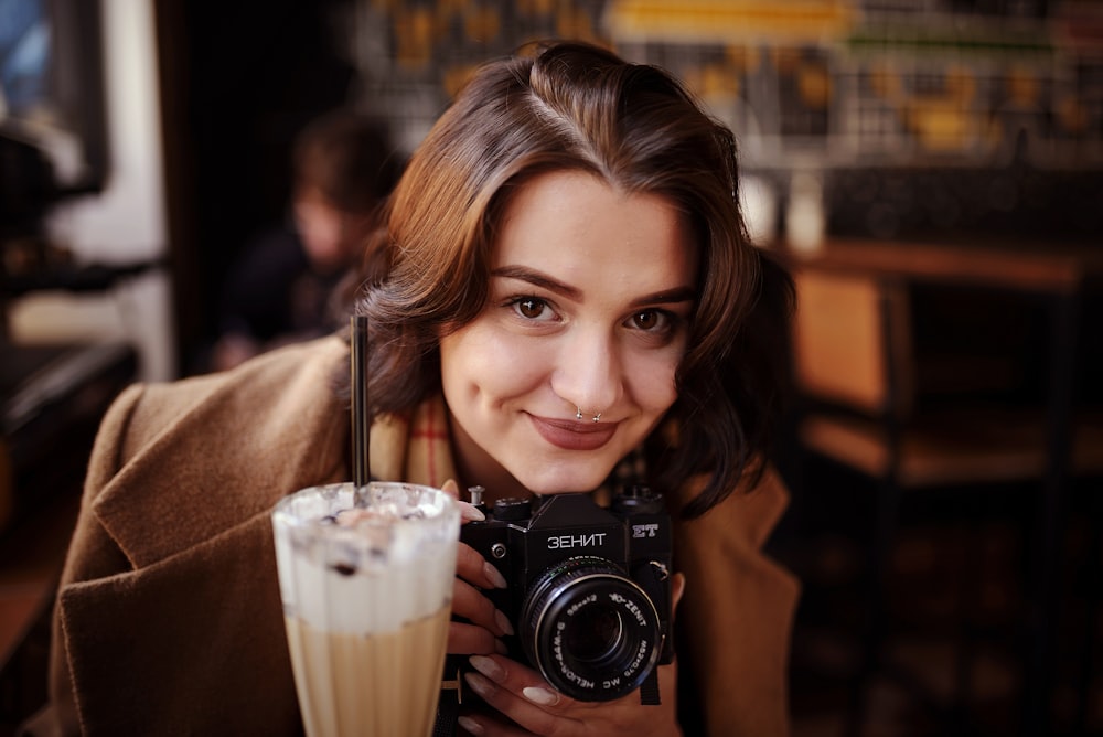 a woman holding a camera and a drink