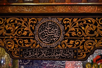 Intricate Arabic calligraphy is surrounded by ornate gold floral patterns on a dark background. The writing includes both circular and rectangular frames. The decorative style is rich and detailed, reflecting traditional artistry.