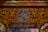 Intricate Arabic calligraphy is surrounded by ornate gold floral patterns on a dark background. The writing includes both circular and rectangular frames. The decorative style is rich and detailed, reflecting traditional artistry.