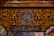 Intricate Arabic calligraphy is surrounded by ornate gold floral patterns on a dark background. The writing includes both circular and rectangular frames. The decorative style is rich and detailed, reflecting traditional artistry.