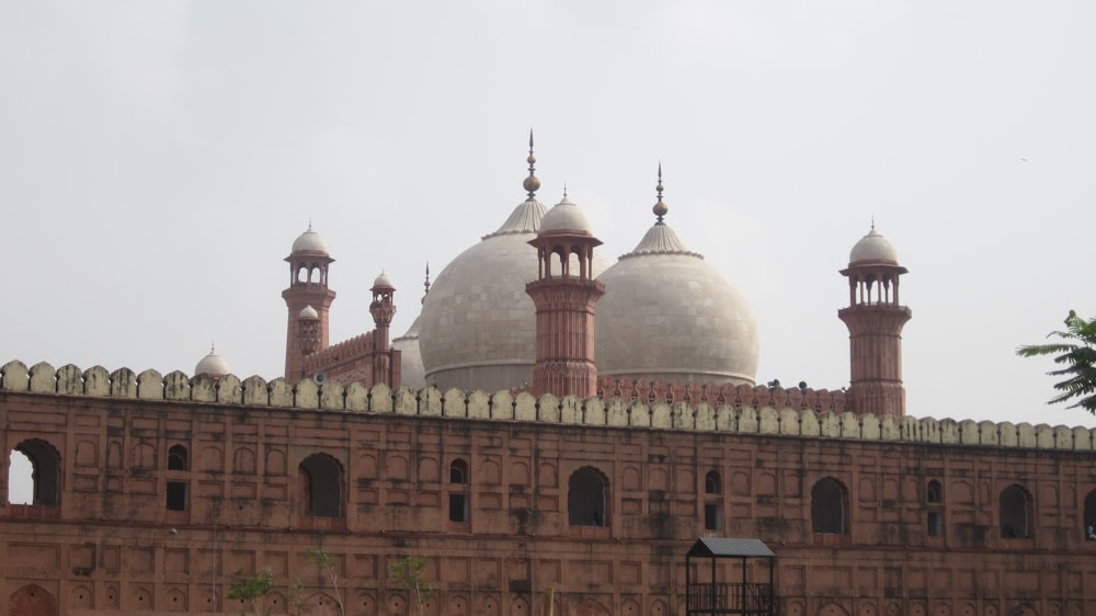 un grande edificio con tetti a cupola con la Moschea Badshahi sullo sfondo