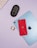 A flat lay of electronic gadgets on a pastel purple background, including a red smartphone, a blue tablet, a black wireless mouse, an SD card, and part of a white keyboard.