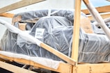 A large object wrapped in bubble wrap is secured within a wooden frame. There are some labels and markings on the packaging, with one label reading 'BURTON'. The object appears to be prepared for shipping or transport.