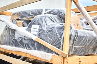 A large object wrapped in bubble wrap is secured within a wooden frame. There are some labels and markings on the packaging, with one label reading 'BURTON'. The object appears to be prepared for shipping or transport.