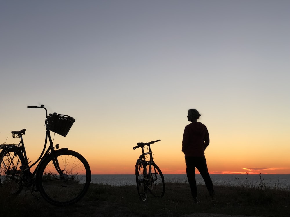 a person standing next to a couple bikes on a beach