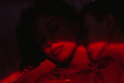 A sensual embrace between a couple, bathed in soft, passionate red lighting.