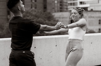 An artistic black and white shot of a couple holding hands in a city street.