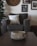 A cozy living room setting with a focus on a textured, rustic bowl on a dark wooden table. In the background, a plush armchair is adorned with a soft white pillow. A large clock and several framed pictures decorate the wall, adding to the warm, homey atmosphere.