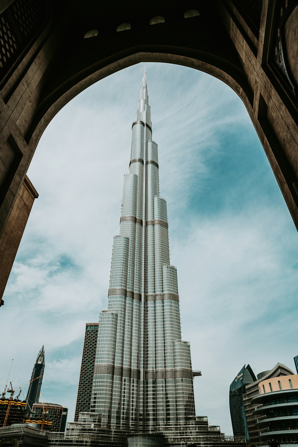 a tall building with a curved top with Burj Khalifa in the background