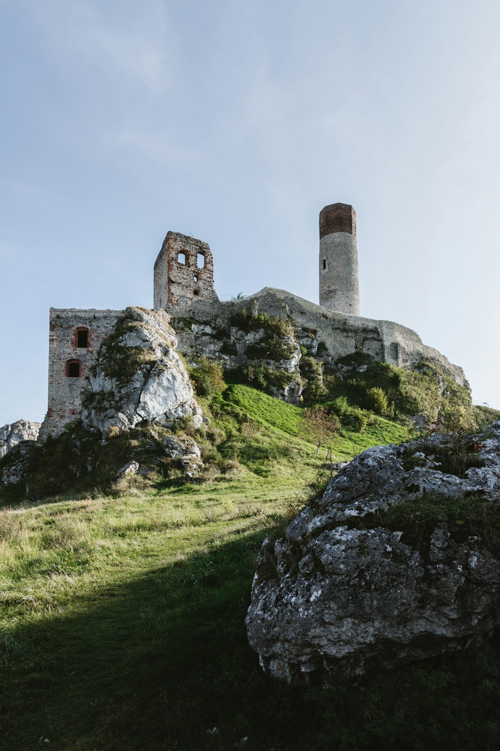 un castillo de piedra en una colina con el castillo de Ogrodzieniec al fondo