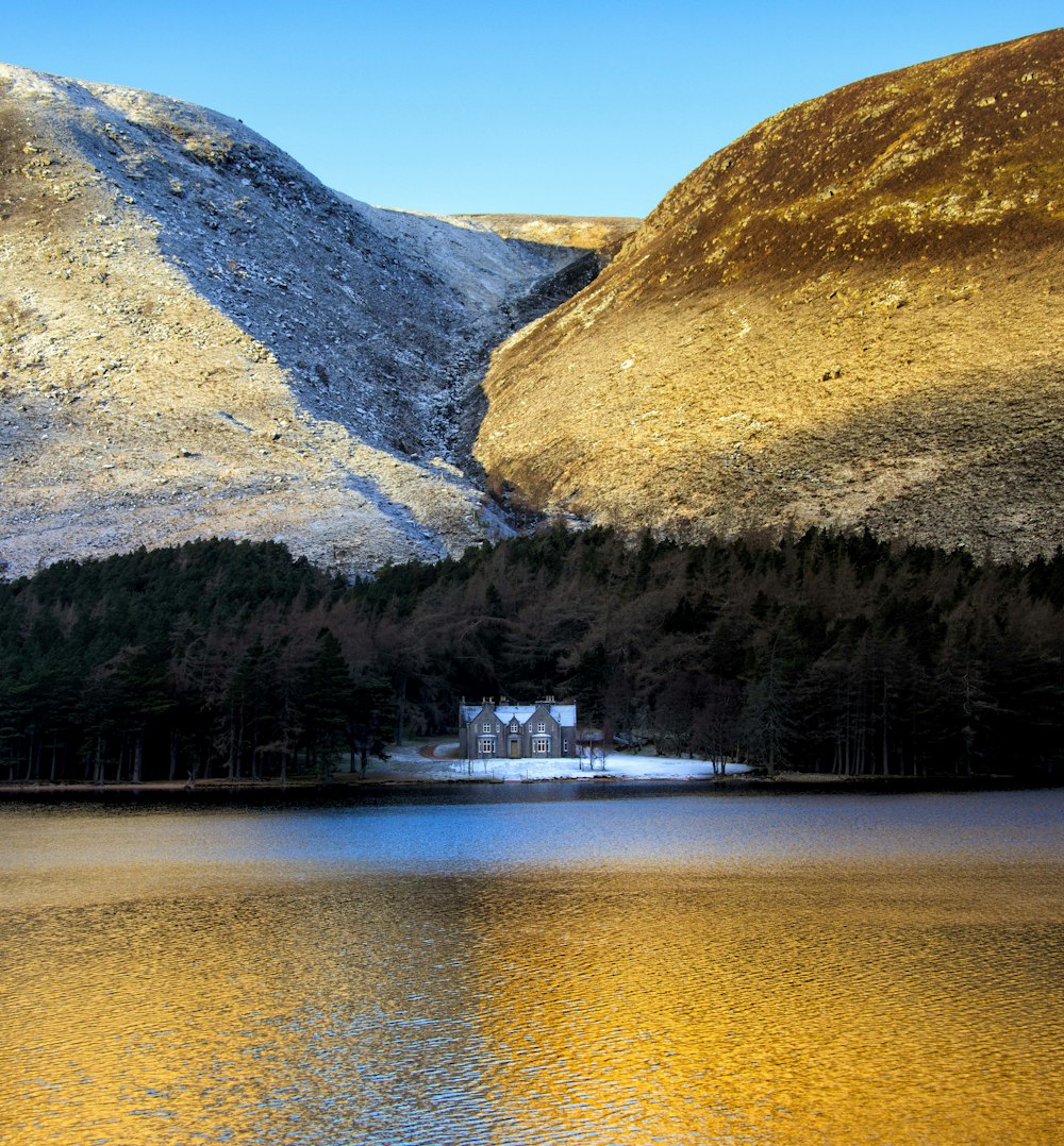 Un edificio en una colina junto a un lago con montañas al fondo