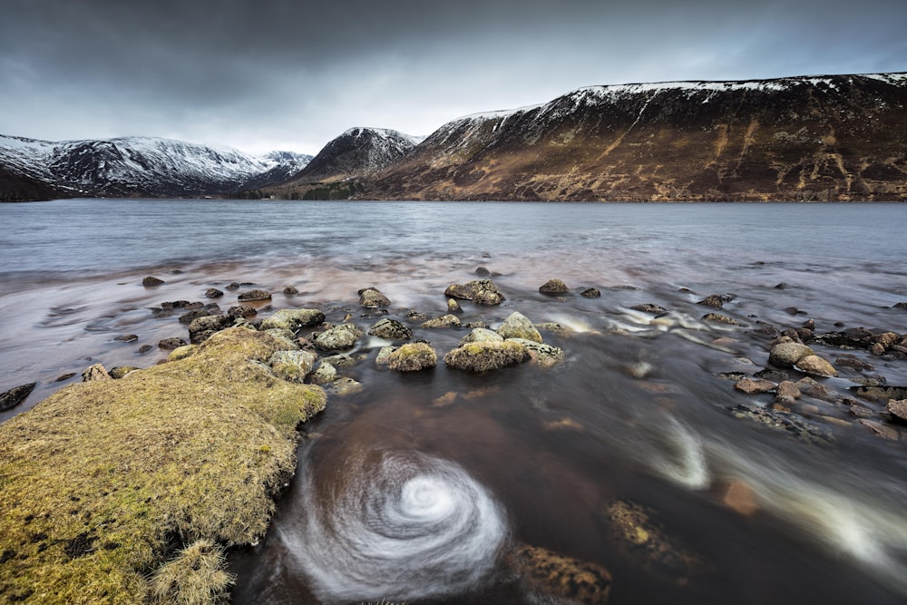 a rocky beach with a body of water and mountains in the background