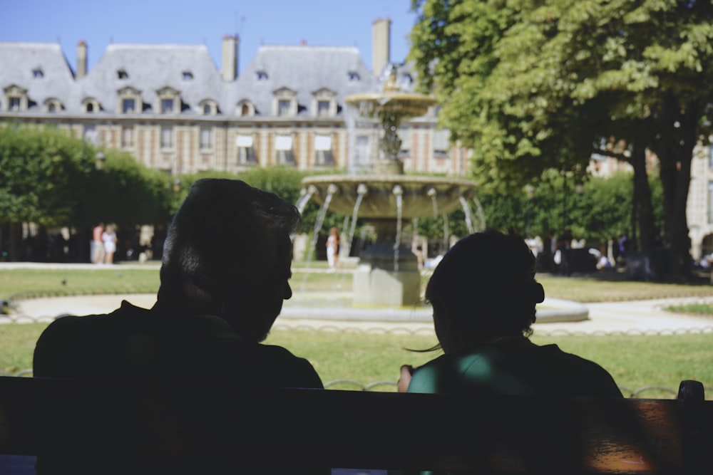 a couple of people sitting in front of a fountain in front of a large building