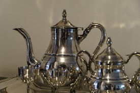 A collection of polished silver tea set items, including a teapot, sugar pot, and a couple of small cups, all with ornate detailing and a reflective surface.