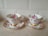 Two ornate teacups with matching saucers featuring a floral design with pink roses. Both cups and saucers have gold decorative accents and are placed on a light-colored countertop in front of a tiled backsplash.