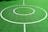 A vibrant green sports court featuring distinct white circular markings and straight lines. The court surface is composed of a textured grid pattern, and small leaves can be seen scattered on the surface.