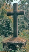 A simple wooden cross resting on smooth stones surrounded by soft moss.