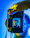A hand holding a Canon camera with a live view screen displaying a portrait of a man wearing glasses. The background is a vibrant mix of blue and yellow tones, creating a striking contrast with the camera's black exterior.