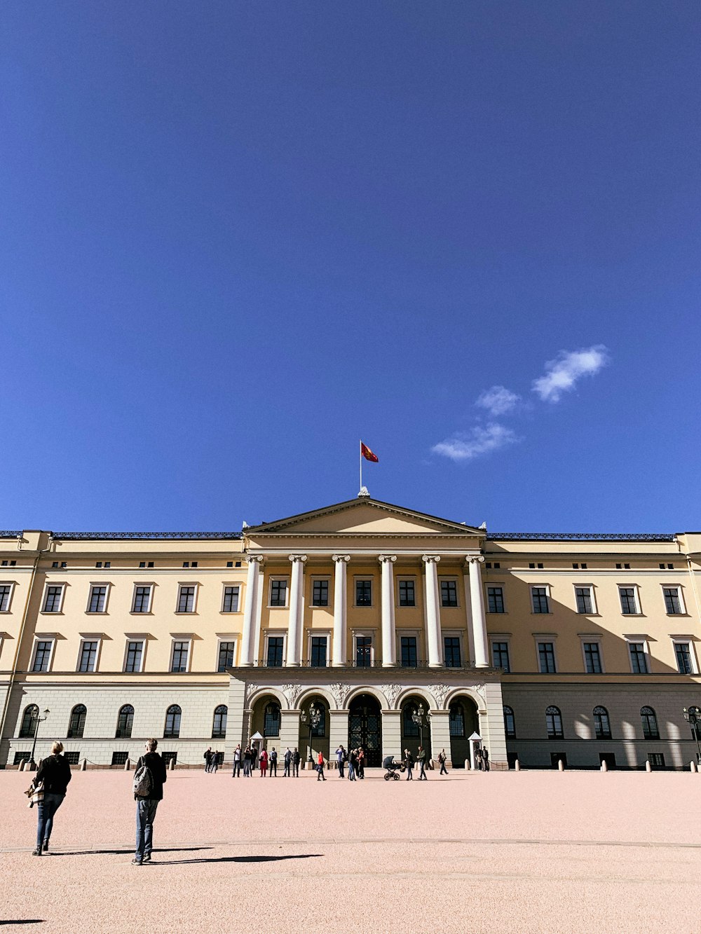 a large building with a flag on top with Royal Palace, Oslo in the background
