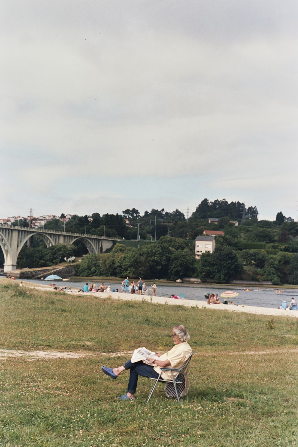 a person sitting in a chair in a grassy field with a bridge in the background